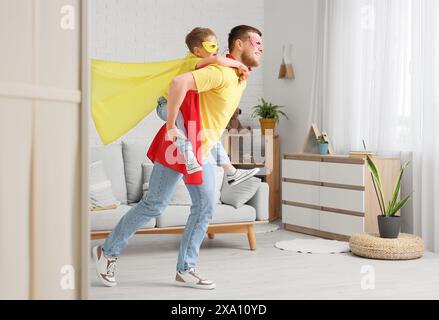 Bambino con suo padre in costumi da supereroe che si diverte a casa Foto Stock