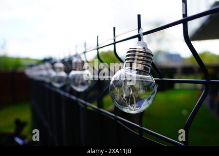 Le lampadine appese su una recinzione metallica vicino a un campo erboso Foto Stock