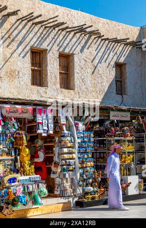 Venditore di abiti tradizionali nel Souq Waqif con la Moschea Fanar sullo sfondo, Doha, Qatar, Asia occidentale Foto Stock