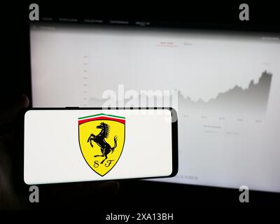 Persona che possiede un telefono cellulare con il logo dell'azienda automobilistica italiana Ferrari Spa di fronte alla pagina web aziendale. Mettere a fuoco il display del telefono. Foto Stock