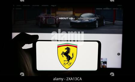 Persona che possiede uno smartphone con il logo dell'azienda italiana di auto sportive Ferrari S.p.A. davanti al sito web. Mettere a fuoco il display del telefono. Foto Stock