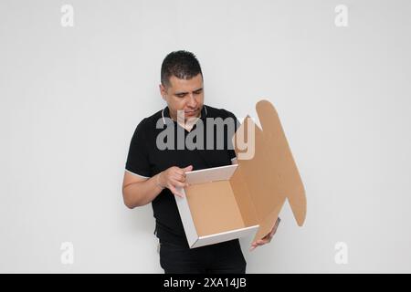 L'uomo adulto latino dalla pelle scura assembla una scatola di cartone seguendo le istruzioni concentrate e attente Foto Stock