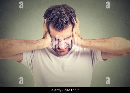 Un giovane infelice e infelice con una t-shirt bianca che stringe la testa con le mani, soffre di mal di testa. Foto Stock