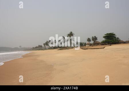 Un tranquillo scenario di una spiaggia sabbiosa costeggiata da palme e tradizionali barche da pesca trainate sulla riva. Piccole capanne sono visibili sullo sfondo Foto Stock