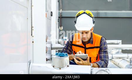 Un lavoratore con attrezzatura di sicurezza e elmetto che utilizza un cellulare in un sito industriale. Foto Stock