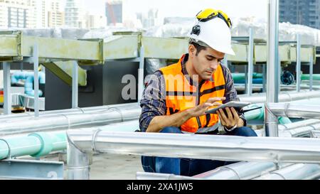 Un uomo con un giubbotto arancione siede sulle pipe, utilizzando uno smartphone. Foto Stock