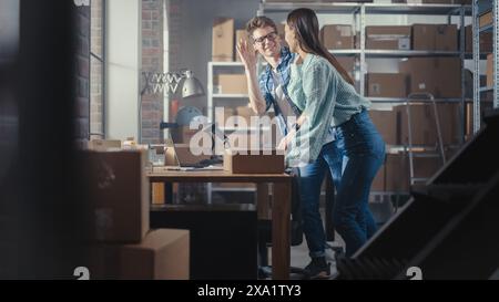 Ritratto di un giovane imprenditore di successo che sorride, guarda la fotocamera. Uomo caucasico che tiene una scatola di cartone in un magazzino con ordini pronti per la spedizione. Foto Stock