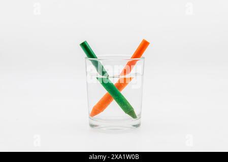 Refracción de la luz, demostrada con un vaso lleno de agua con lápices de colores Foto Stock