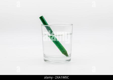 Refracción de la luz, demostrada con un vaso lleno de agua con lápices de colores Foto Stock