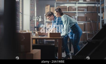 Due dipendenti che preparano gli ordini effettuati dalle vendite online nel loro negozio Internet. Uomo e donna che lavorano in un magazzino. Giovane donna che utilizza un computer portatile, l'uomo che imballa gli oggetti. Messa a fuoco rack. Foto Stock