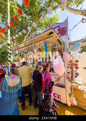 I visitatori del festival indossano abiti tradizionali al Feira de Abril di Siviglia, facendo la fila a un venditore di dolci durante il festival della durata di una settimana Foto Stock