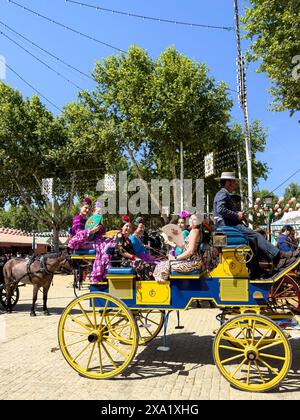 Donne in abiti tradizionali di flamenco su una carrozza trainata da cavalli alla Feria de Abril, nota anche come la Fiera di Siviglia Foto Stock