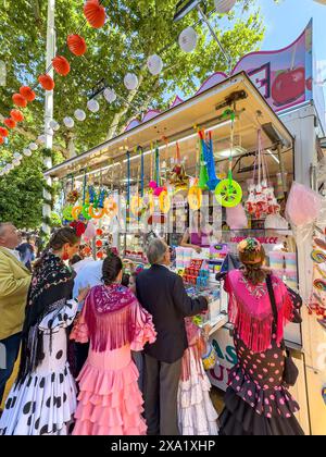 I visitatori del festival indossano abiti tradizionali al Feira de Abril di Siviglia, facendo la fila a un venditore di dolci durante il festival della durata di una settimana Foto Stock