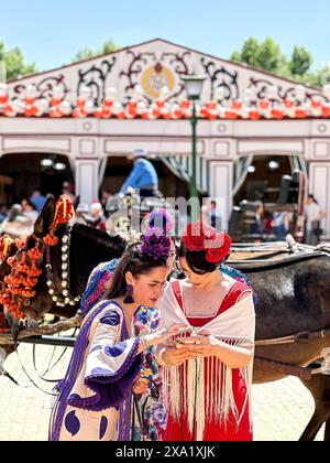 Due donne in abiti di flamenco vicino a una carrozza trainata da cavalli alla Feria de Abril, nota anche come la Fiera di Siviglia Foto Stock