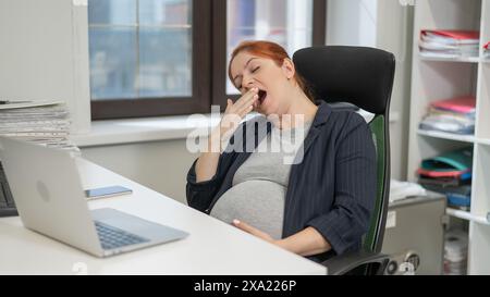 Donna incinta che dorme alla sua scrivania in ufficio. Foto Stock