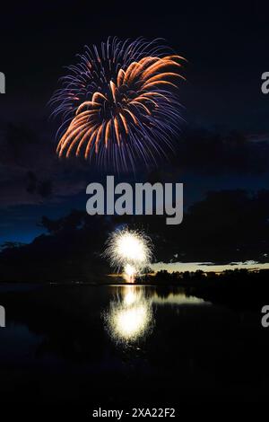 I colorati fuochi d'artificio illuminano il cielo notturno sopra un sereno corpo d'acqua Foto Stock