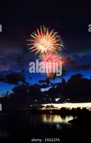 I colorati fuochi d'artificio illuminano il cielo notturno sopra l'acqua, con edifici cittadini sullo sfondo Foto Stock