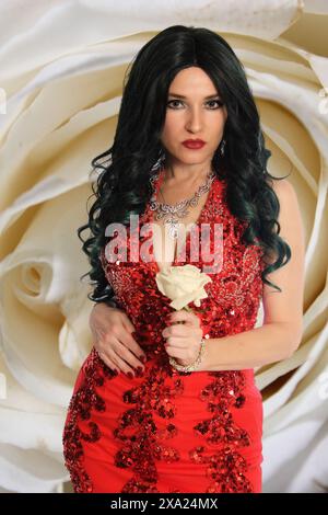 Una donna con un vestito rosso che posa con una rosa bianca Foto Stock