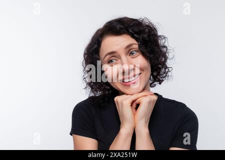 Una modesta bruna con capelli ricci indossa una maglietta nera su uno sfondo con spazio di copia Foto Stock