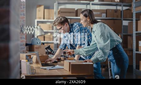 Due dipendenti che preparano gli ordini effettuati dalle vendite online nel loro negozio Internet. Uomo e donna che lavorano in un magazzino. Giovane donna che utilizza un computer portatile, l'uomo che imballa gli oggetti. Messa a fuoco rack. Foto Stock