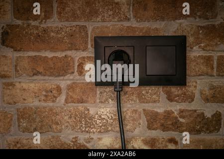 Immagine ravvicinata di una presa elettrica nera montata su una parete in mattoni Foto Stock