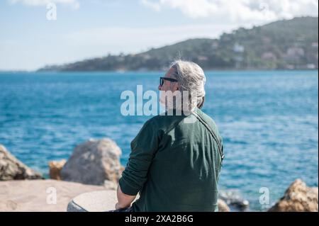 Un uomo anziano seduto sulla riva della città portuale toscana di Porto Santo Stefano in Italia Foto Stock