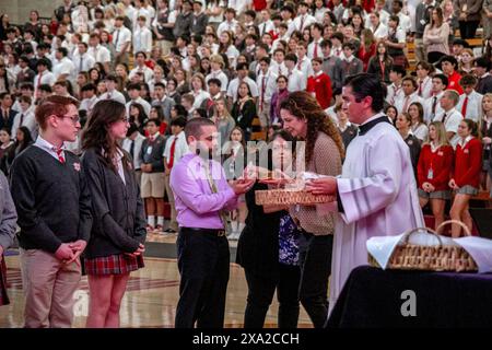 Gli studenti multirazziali di una scuola superiore cattolica della California meridionale presentano l'ospite ad un sacerdote prima della comunione durante una messa scolastica nel gy Foto Stock