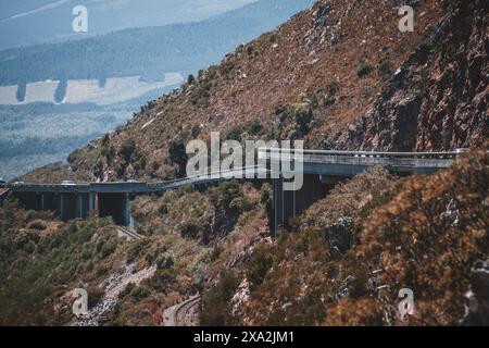 Una vista mozzafiato di una tortuosa autostrada di montagna in Sud Africa, con auto che percorrono la strada sopraelevata sullo sfondo di aspre colline e lussureggianti Foto Stock