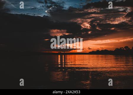 Un'immagine impressionante che cattura un tramonto ardente sul fiume Zambesi con vivaci sfumature di arancione e rosso che si riflettono sull'acqua creando un mesmeriz Foto Stock