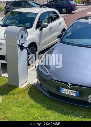 Cremona, Italia - 2 maggio 2024 due auto elettriche, una tesla e una fiat, si stanno caricando in una stazione di ricarica pubblica, evidenziando la crescente popolarità Foto Stock