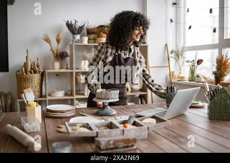 ceramista femminile che lavora in studio di ceramica utilizzando un computer portatile Foto Stock