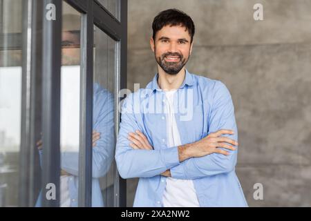 Uomo sicuro di sé in piedi con le braccia incrociate vicino alla porta di vetro Foto Stock