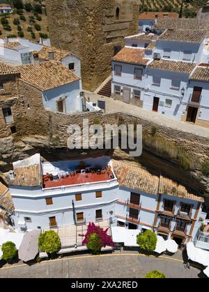 Primo piano di case integrate tra pareti di roccia con terrazza e piante fiorite in primo piano, vista aerea, abitazioni nelle grotte, Setenil de las Foto Stock