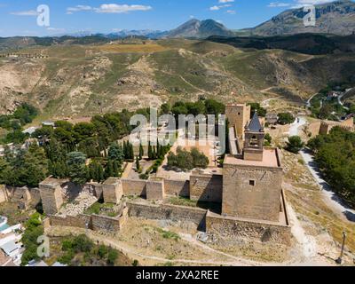 Vista aerea di una fortezza storica, circondata da alberi e montagne, con imponenti mura e torri, dall'alto dalla vegetazione con il sole Foto Stock