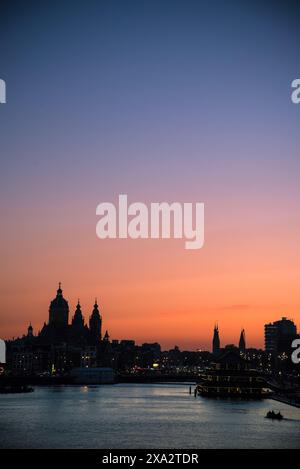Tramonto sul fiume IJ con la sagoma della basilica di San Nicola in lontananza - Amsterdam, Paesi Bassi Foto Stock