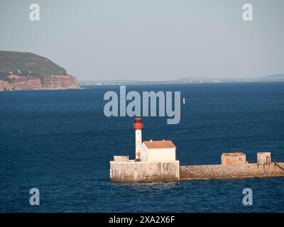 Faro bianco con tetto rosso si erge su un molo nel mare blu calmo sotto un cielo limpido, la seyne sur Mer, francia Foto Stock