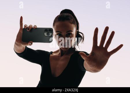 La ballerina e la creatrice di contenuti si registra ballando in uno studio. Tenendo in mano uno smartphone, cattura le sue mosse espressive in un selfie a specchio. Con un foc Foto Stock