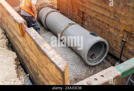 Costruttore installazione di un tubo di drenaggio in calcestruzzo di grande diametro protetto da un sistema di supporto per trincee durante lavori di drenaggio profondo Foto Stock