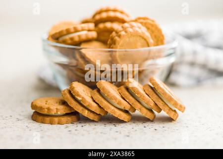 Uno shot ravvicinato di una ciotola di vetro traboccante di biscotti dorati. Alcuni biscotti sono disposti sul bancone a destra della ciotola, cre Foto Stock