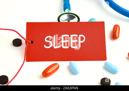 Simbolo sonno profondo. Parola SONNO scritto su un biglietto rosso su uno stetoscopio con pillole sulla superficie Foto Stock