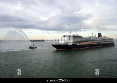 Queen Anne, la nuova nave da crociera di lusso gestita da Cunard, che naviga sul Solent vicino a Southampton con una guardia d'onore da un Tug Boat antincendio. Foto Stock