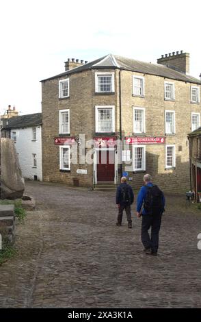 Uomini (escursionisti) a piedi fino al George & Dragon Hotel vicino alla Adam Sedgwick Memorial Fountain nel villaggio di Dent nel Parco Nazionale delle valli dello Yorkshire. Foto Stock