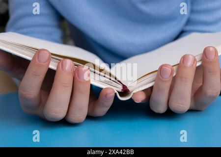 Unghie pastello morbide e curate con taccuino di carta su sfondo blu. Donna che mostra la sua nuova manicure nei colori della tavolozza pastello. Decorazioni semplici, fresche vibrazioni primaverili dai colori naturali Foto Stock