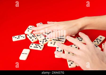 Mani maschili che mescolano domino. pezzi acrilici. Isolato su sfondo rosso. Foto Stock