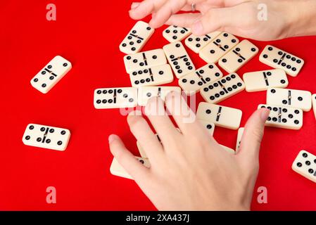 Mani maschili che mescolano domino. pezzi acrilici. Isolato su sfondo rosso. Foto Stock