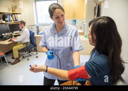 Infermiere che prende la pressione sanguigna del paziente in una clinica, medico in background Foto Stock