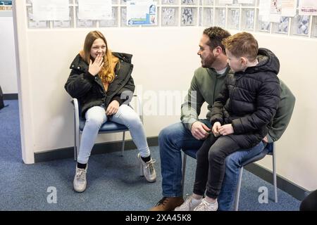 Tre persone sedute in sala d'attesa di uno studio medico, padre, figlio e figlia Foto Stock