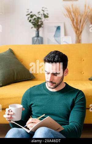 Uomo che scrive su un taccuino su un divano giallo Foto Stock