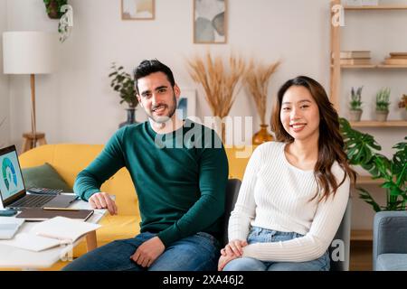 Uomo e donna sorridenti seduti su un divano giallo con un portatile Foto Stock