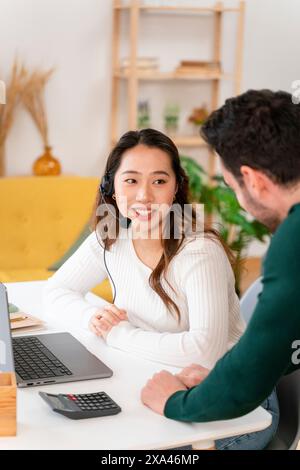 Giovane donna con cuffie alla scrivania che parla con un uomo Foto Stock
